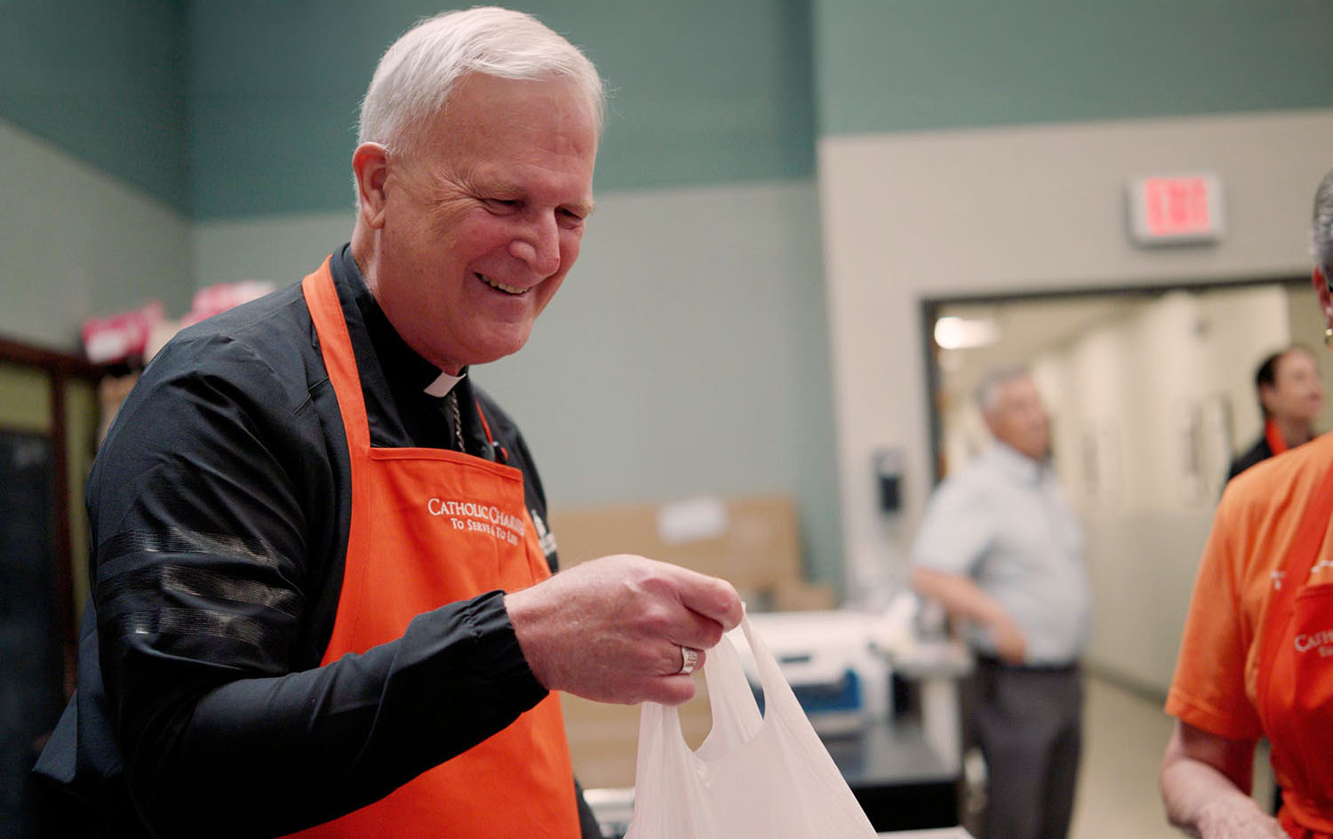 Bishop smiling, holding donation bag