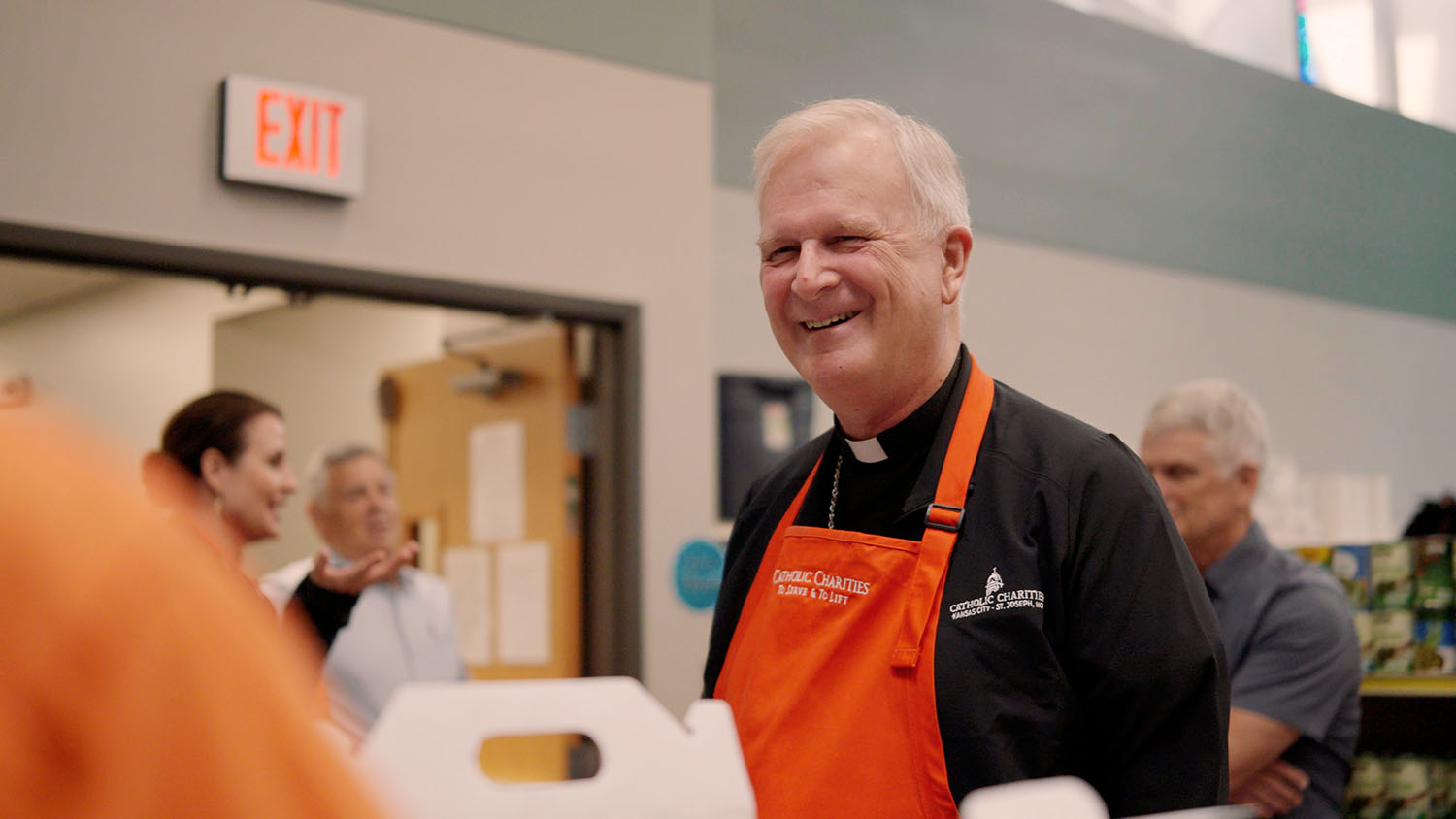 Bishop smiles while wearing Catholic Charities apron