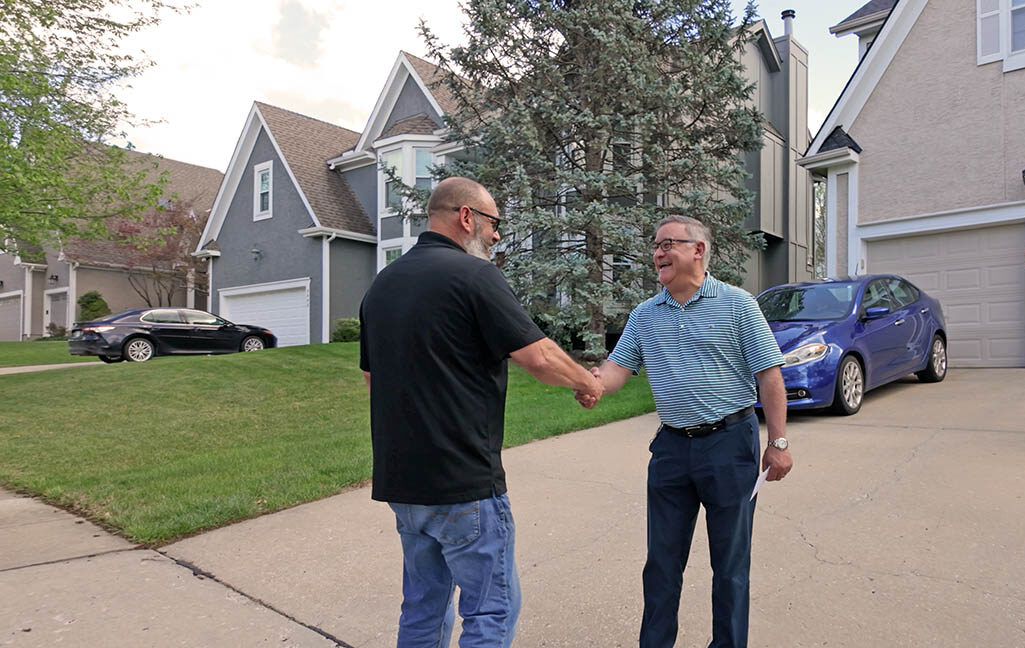 Two men shake hands outside a house.