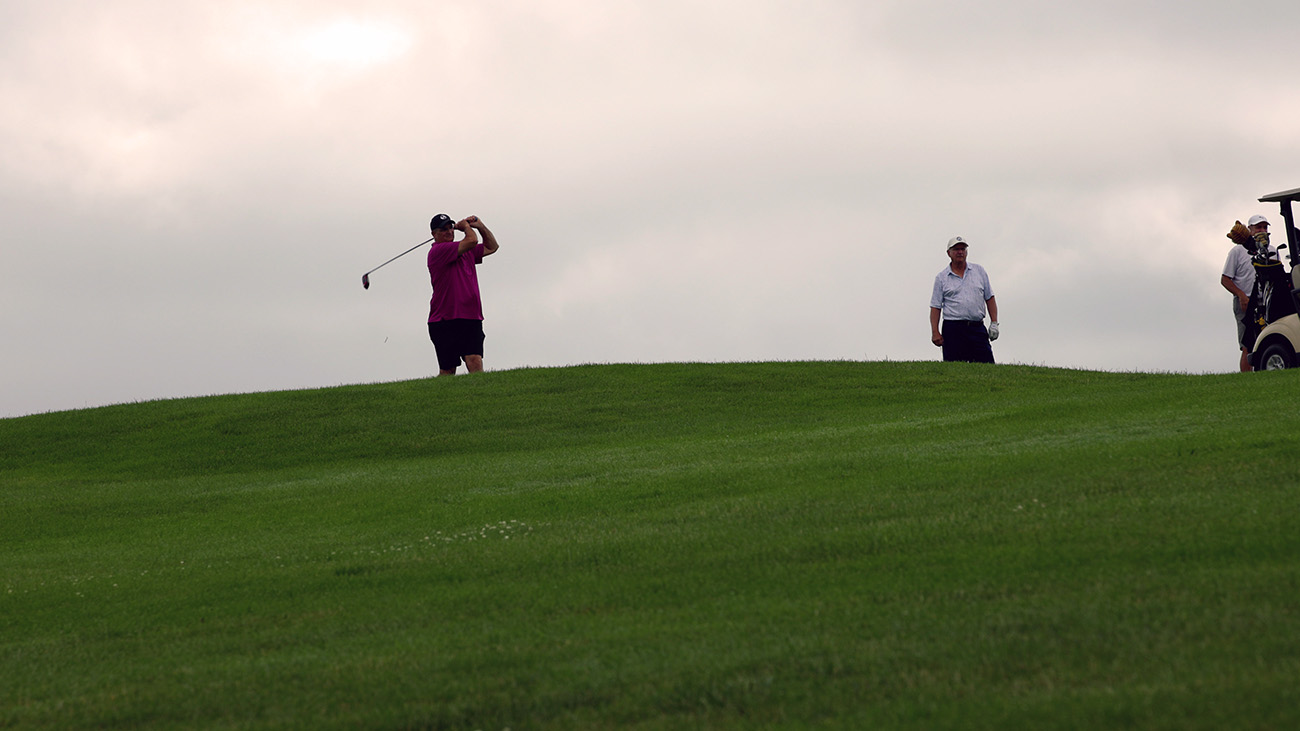 Golfer swings club on green hill