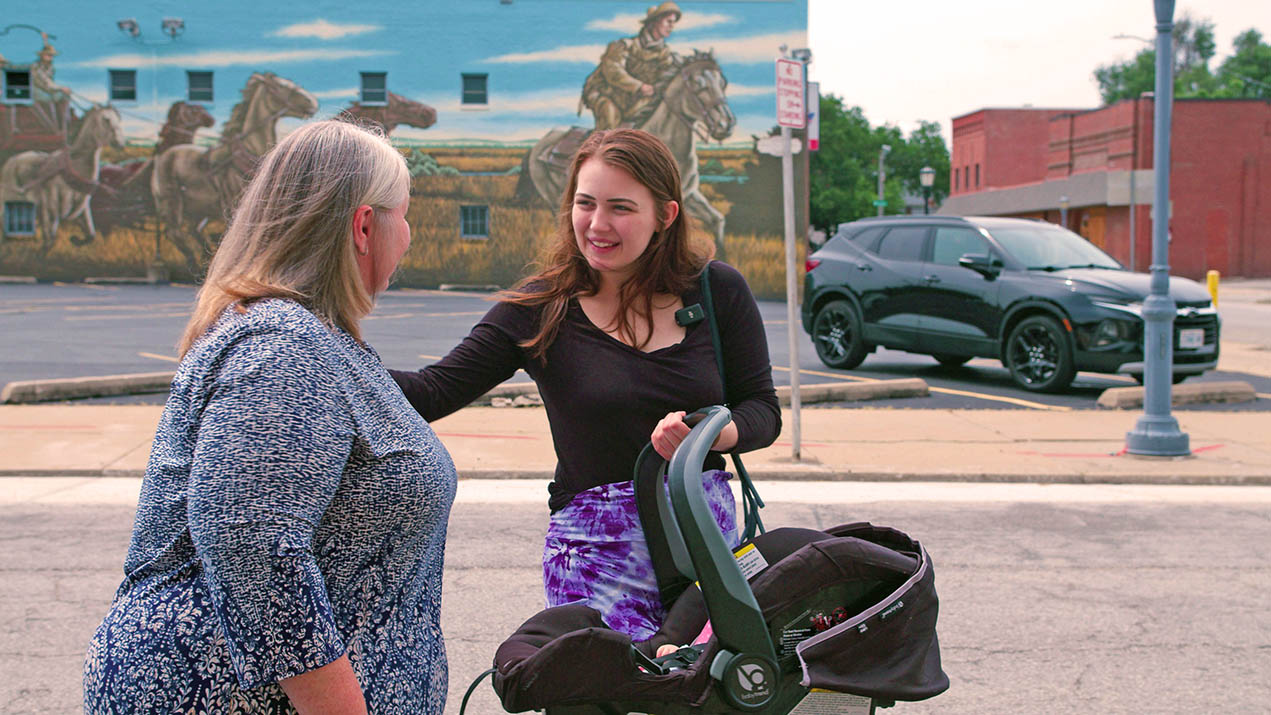 Woman with baby carrier talks to another woman