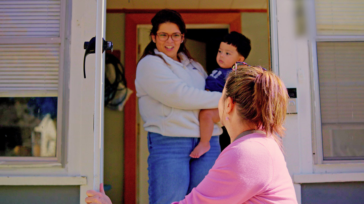 Woman holds baby, greets visitor at door