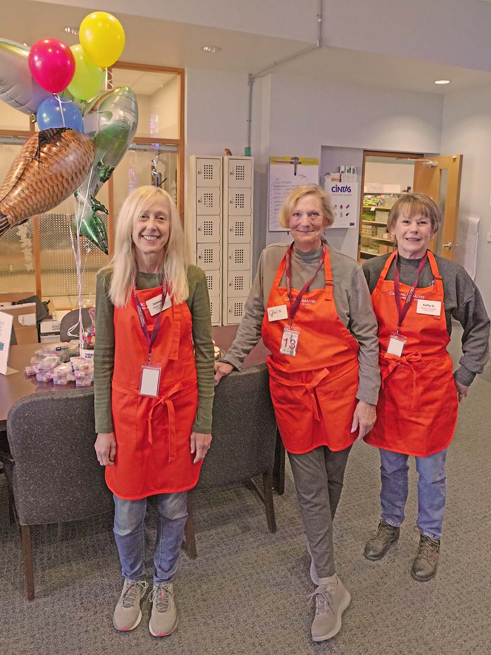 Three women in orange aprons smiling