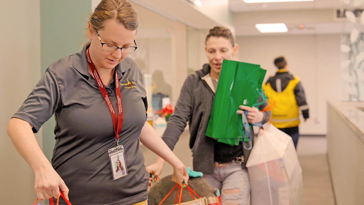 A woman helps another woman carry packages