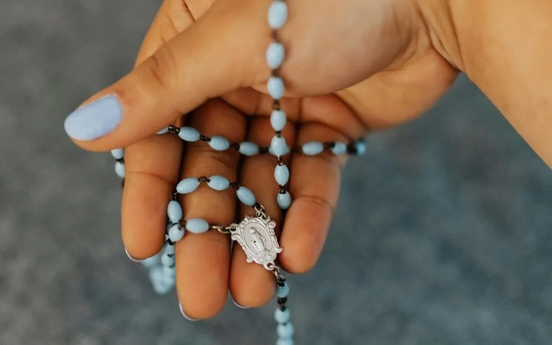 Hand holding blue rosary beads